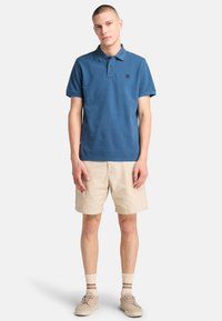 Mörkblå pikétröja med korta ärmar och en liten logotyp, tillsammans med beiga shorts. Tyget har en slät textur och klassisk passform.