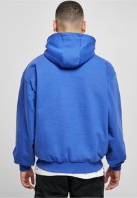 Sudadera con capucha azul con una capucha grande y ajustable. Presenta un ajuste holgado, puños y cinturilla acanalados. Textura suave y color uniforme.