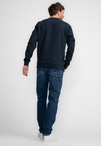 Marineblauw sweatshirt met lange mouwen, ronde hals en ribgebreide manchetten, gecombineerd met donkerblauwe jeans en witte schoenen. Eenvoudige, casual stijl.