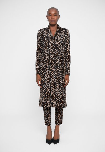 Black and beige geometric patterned outfit with a long coat and cropped pants, made of smooth fabric, featuring a collar and button detail.