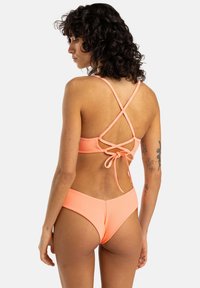 Bikini komplet v malinasti roza barvi z teksturirano tkanino, križnimi zankami na hrbtni strani in srednje visokimi hlačkami z gladkim zaključkom.