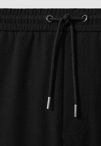 Sorte shorts med elastisk talje, der har en snor med sølvspidser. Glat tekstur, med synlig syning og en sidelomme.