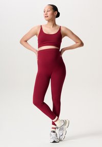Bordeauxroze sportieve cropped top en hooggetailleerde leggings gemaakt van rekbare stof, gecombineerd met grijze sneakers en gestreepte witte en rode sokken.