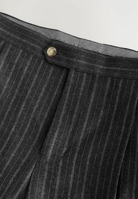 Gray pinstriped trousers made of textured fabric, featuring a front button closure and pleats, with a contrasting herringbone interior lining.