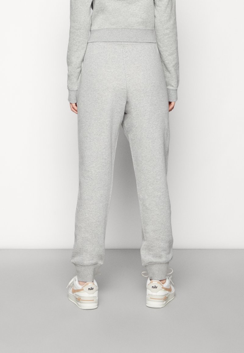 Graue Sweatpants mit entspannter Passform, bügelbaren Knöcheln, weicher Textur und kombiniert mit weißen Sneakern mit orangefarbenen und schwarzen Akzenten.