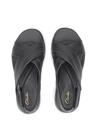 Sandales en cuir noir avec des brides croisées, semelle intérieure rembourrée et semelle extérieure blanche. Possède des perforations pour la respirabilité et la marque "Clarks".