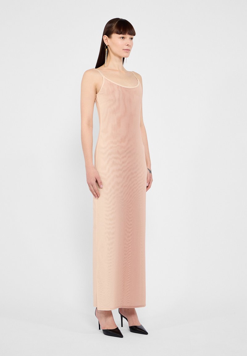 Robe maxi nude sans manches avec une texture lisse, dotée d'un décolleté arrondi et d'une coupe ajustée, associée à des escarpins noirs à bout pointu.
