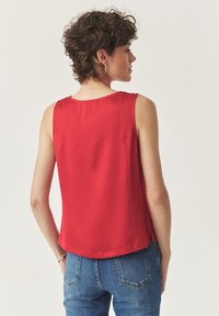 Rode mouwloze blouse van een soepel, lichtgewicht stof. Heeft een ronde halslijn en zijsplitten aan de zoom. Achteraanzicht getoond.