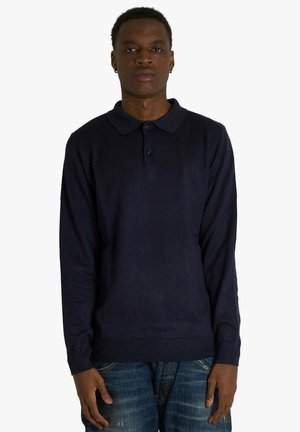 Polo a maniche lunghe color blu marina realizzato in tessuto morbido, con colletto, tre bottoni e polsini a coste. Abbinato a jeans in denim.