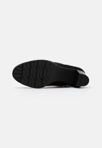 Schwarze Schuhsohle mit strukturierten Profilen für Halt, verstärkte Zehenpartie und gebogene Ferse. Flaches Design und matte Oberfläche.
