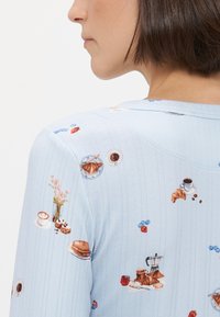 Svijetloplav gornji dio s dugim rukavima i teksturalnim rebrastim detaljima, s razigranim uzorkom kave, peciva i cvijeća.