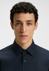 Marinblå skjorta med knappar, med en vikkrage, slät textur och subtil lyster. Har kontrasterande knappar och en skräddarsydd passform.