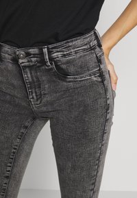 Zwarte denim jeans met een fitted ontwerp, voorzien van een knoopsluiting, vijf zakken en een subtiele vervaging in de stof.