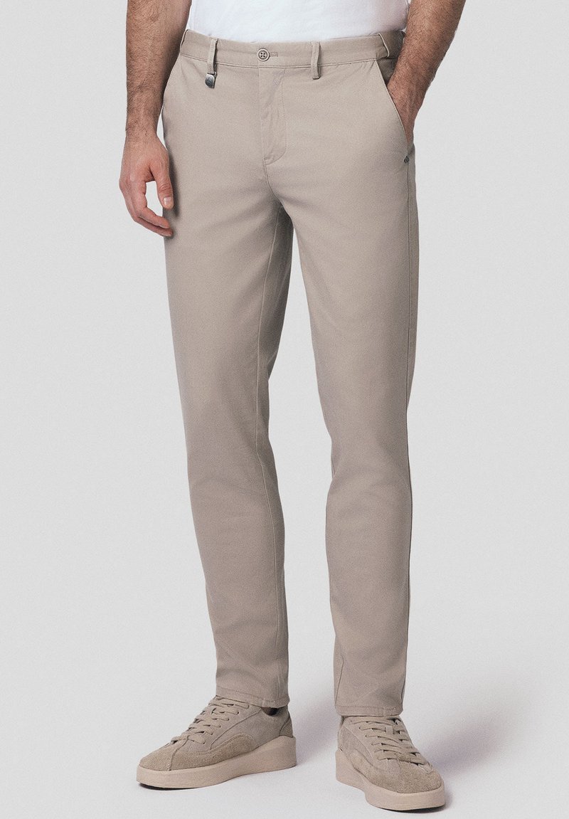 Beżowe chinosy wykonane z miękkiej tkaniny, w wąskim kroju, z ukośnymi kieszeniami i pojedynczym zapięciem na guzik, z subtelnymi detalami szycia.