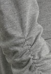 Gray fabric with a soft texture featuring gathered stitching along the sleeve for a fitted look. Simple, casual design.