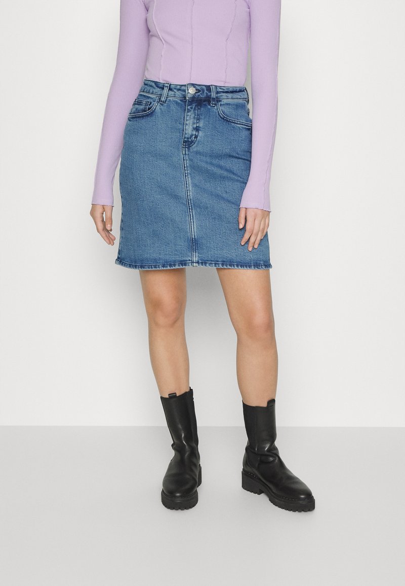 Saia de ganga em azul claro, com formato A-line e bainha desfeita. Apresenta dois bolsos frontais, passantes para cinto e fecho com botão prateado.