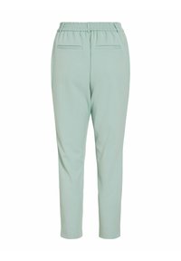 Pantalon vert clair fuselé avec ceinture élastique et deux poches passepoilées arrière, vu de dos sur fond blanc.