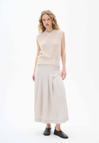 Beiges ärmlös stickad topp med V-ringning, kombinerad med en ljusbeige plisserad maxikjol. Svarta slip-on skor fulländar outfiten.