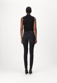 Top negro sin mangas combinado con jeans ajustados negros. Los jeans tienen un diseño de cinco bolsillos y detalles de costura sutiles, llevados con tacones negros.