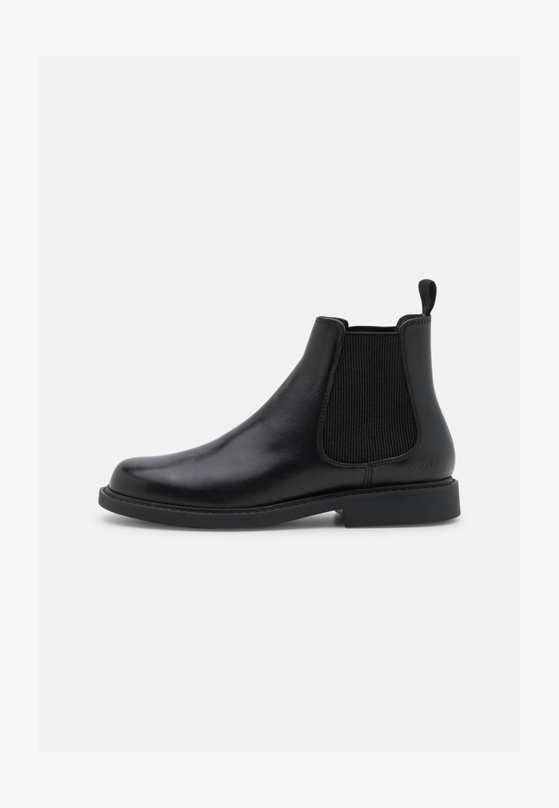 Bota Chelsea preta em couro com painéis laterais elásticos, bico arredondado, sola plana em borracha e uma alça na parte de trás. Textura suave no geral.