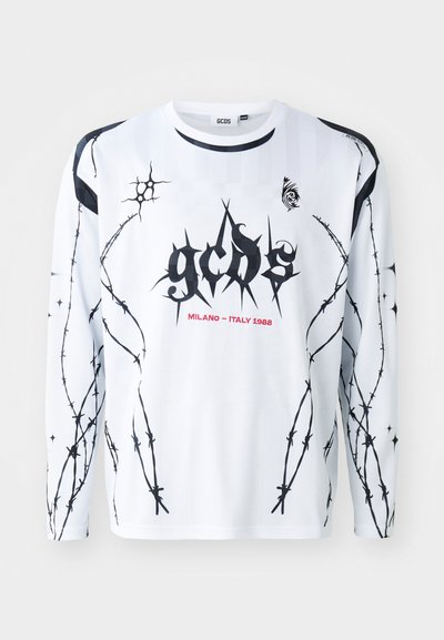 Valkoinen pitkähihainen paita mustilla piikkilanka grafiikoilla ja "GCDS" tekstillä. Sisältää punaisen "MILANO - ITALY 1988" yksityiskohdan ja mustat korostukset hihoissa.