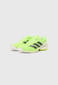Jasnozielone buty sportowe z czarnymi paskami i białą podeszwą. Posiadają siateczkową cholewkę i teksturowaną podeszwę zapewniającą przyczepność.