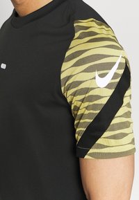 Svart atletisk t-shirt med korta ärmar. Vänster ärm har ett mönster av gula och svarta tigerränder med en vit Nike-logotyp. Slät textur.