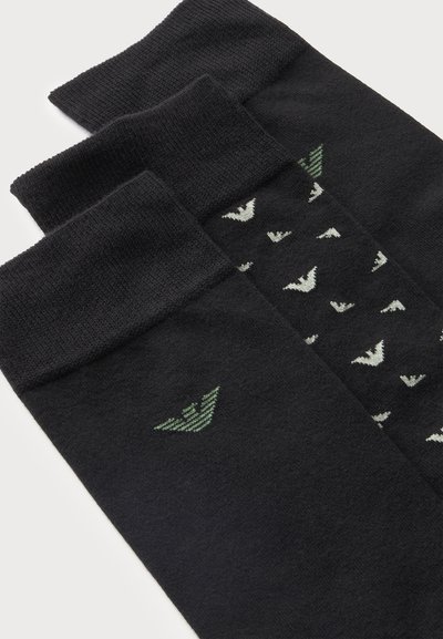Trois paires de chaussettes noires, dont une paire avec de petits motifs d'oiseaux blancs et une autre avec un logo d'oiseau vert près du bord-côte.