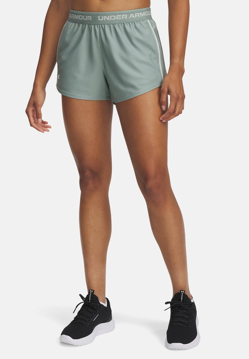 Žalios sportinės šortai su plačiu juosmeniu, kuriame yra "Under Armour" užrašas, šoninėmis juostelėmis ir lygiu, lengvu audiniu.
