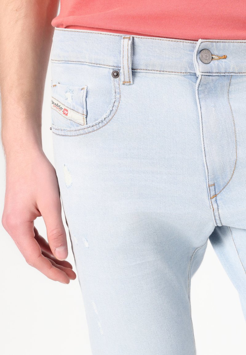 Hellblaue Jeans im Slim-Fit-Schnitt, mit einer ausgewaschenen Textur, distressed Details und orangefarbenen Nähten. Mit einem kleinen roten Etikett an der Gesäßtasche.