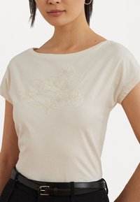 Light beige short-sleeved t-shirt with a soft, smooth texture featuring embroidered floral design on the front and a wide neckline.