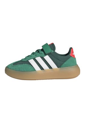 Zielony but sportowy Adidas z białymi paskami, gumową podeszwą, czerwoną pętelką na pięcie, sznurowadłami i zielonym paskiem na rzep na białym tle.