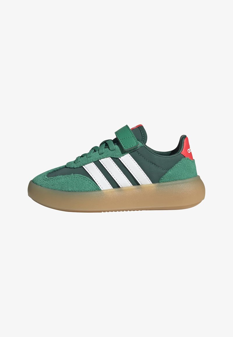 Green Adidas sneaker with white stripes, gum sole, red heel tab, laces, and a green velcro strap on a white background.