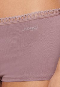 Shorty Sloggi en tissu mauve doux, présentant une taille en dentelle décorative et un logo subtil, texture lisse et forme ajustée.