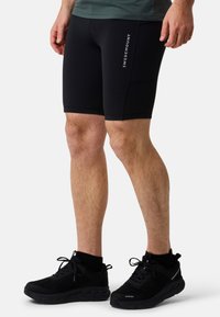 Shorts de sport noirs en tissu extensible, avec un design ajusté. Logo "Swedemount" en blanc sur la jambe gauche. Chaussures de course noires avec des détails en mesh.