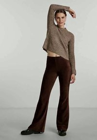 Brauner kurzer Pullover mit strukturiertem Strickdesign, kombiniert mit hochgeschnittenen braunen Schlaghosen aus einem weichen Stoff.