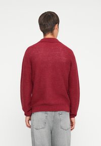 Maroon knit sweater with a relaxed fit, featuring a textured pattern, long sleeves, and a collar; paired with gray wide-leg jeans.