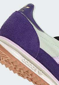 Fialové semišové a mentolovo zelené textilné tenisky s bielou medzipodrážkou a ružovými akcentmi. Obsahujú štruktúrovaný povrch a embosované logo na päte.