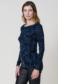 Camiseta de manga larga en negro con un patrón floral azul. Presenta un escote barco y una silueta ajustada, hecha de un tejido de punto suave.
