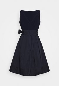 Mustat hihattomat midi-mekko V-pääntiellä, tiukka vyötärö, jonka ympärille on sidottu nauha, ja levenevä laskostettu hame.