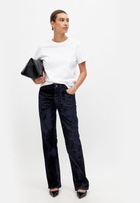 Navy velvet wide-leg trousers paired with a plain white t-shirt and black clutch, complemented by pointed black heels and sleek hair.