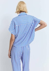 Camicetta a maniche corte e pantaloni abbinati in righe verticali azzurre e rosa. Vestibilità morbida e rilassata con colletto e maniche ampie.
