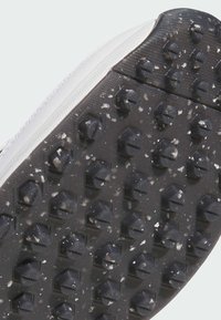 Black rubber shoe sole featuring hexagonal studs for traction, with a white edge. Surface shows dirt and wear.