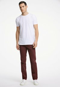 Witte katoenen T-shirt, slim fit, gecombineerd met bordeauxrode chinos. Model draagt witte sneakers. Eenvoudig ontwerp zonder patronen of hardware-details.