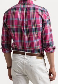 Rutig skjorta i rosa och blått med upprullade ärmar, med en plissering bak. Bärs med vita byxor och ett brunt bälte.