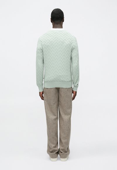 Pull vert menthe avec un motif texturé, doté d'un col blanc. Associé à un pantalon ample marron clair.