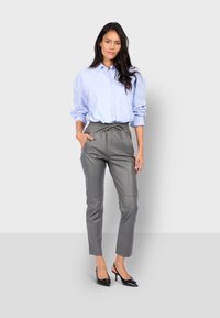 Šedé kožené kalhoty s elastickým pasem, spárované se světle modrou košilí na knoflíky. Oblečení se vyznačuje neformálním stylem a přiléhavou siluetou.