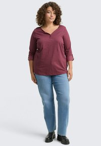 Rode katoenen shirt met 3/4 mouwen en een V-hals, met een geruit patroon. Gekenmerkt door lichtblauwe jeans en zwarte enkelboots.