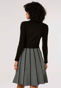 Haut noir à manches longues côtelé associé à une jupe évasée à motif chevrons noir et blanc, mettant en valeur des textures et motifs contrastés.