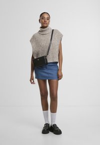 Pull à col roulé en beige avec des paillettes multicolores, associé à une mini-jupe en jean bleu. Sac bandoulière noir, chaussettes blanches et mocassins noirs.